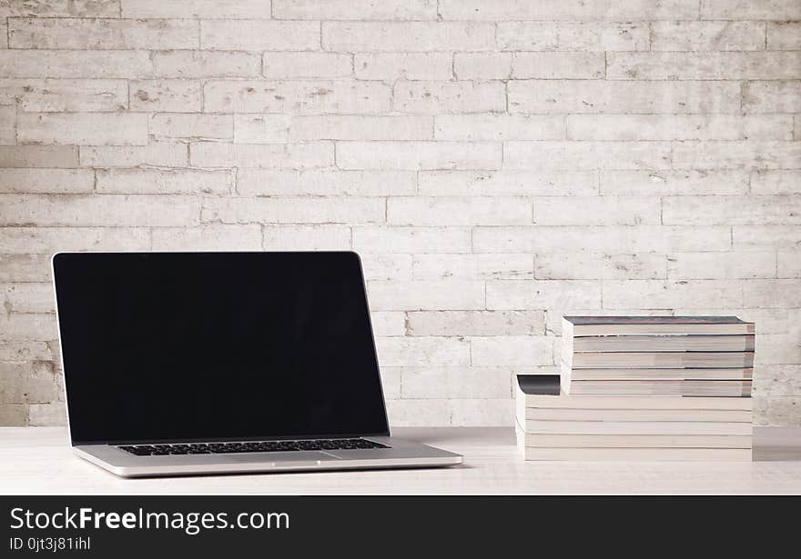 An open laptop on an office desk with flower, coffee, books in front of white brick wall background concept. An open laptop on an office desk with flower, coffee, books in front of white brick wall background concept