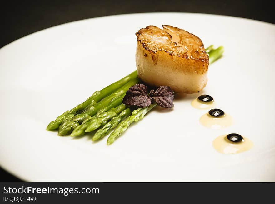 Scallop with green asparagus on white plate