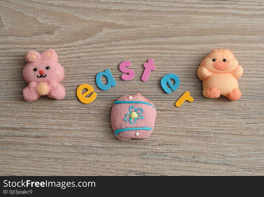 A pink bunny shape marshmallow, a chicken shape marshmallow and an egg with the word easter on a wooden background