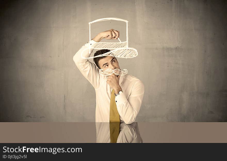 A young happy businessman in elegant suit drawing funny hat and mustache in empty grey space with a chalk illustration concept. A young happy businessman in elegant suit drawing funny hat and mustache in empty grey space with a chalk illustration concept