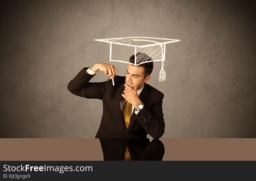 An elegant, successful university student drawing himself a square academic mortarboard cap with a chalk in front of grey wall background concept. An elegant, successful university student drawing himself a square academic mortarboard cap with a chalk in front of grey wall background concept