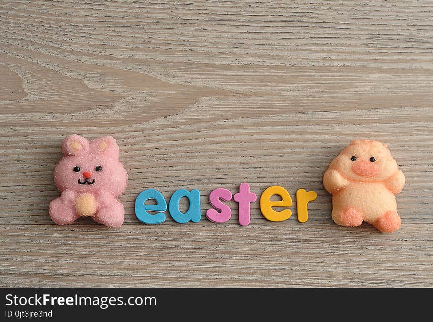 A pink bunny shape marshmallow and a chicken shape marshmallow with the word easter isolated on a wooden background