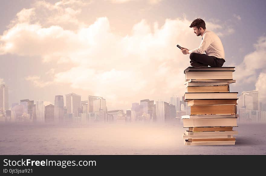 A serious student with laptop tablet in elegant suit sitting on a stack of books in front of cityscape with clouds. A serious student with laptop tablet in elegant suit sitting on a stack of books in front of cityscape with clouds