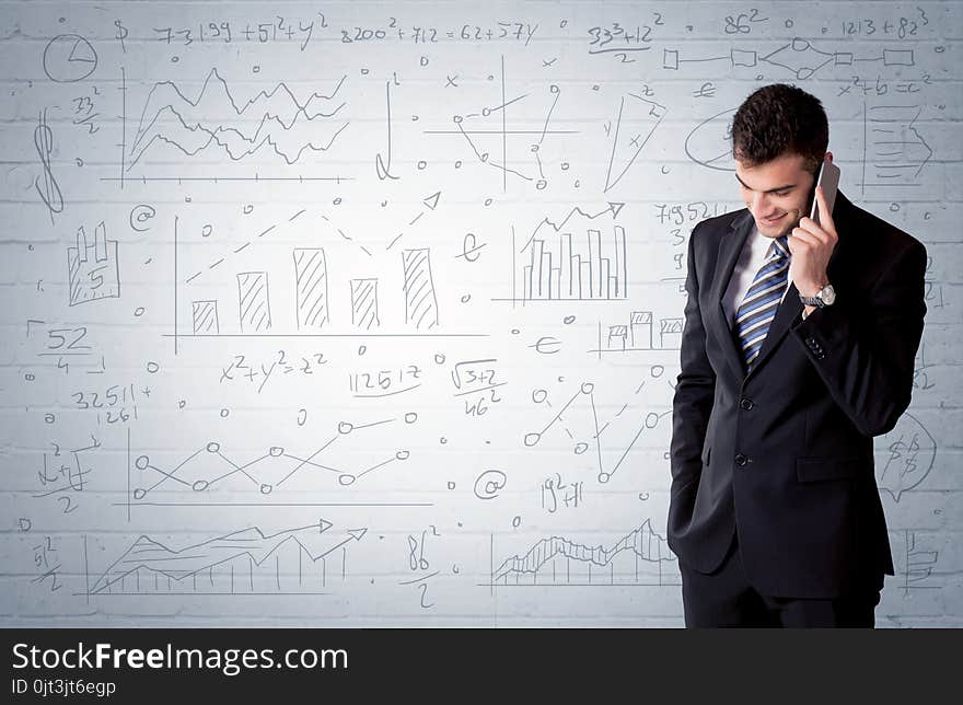 A confident young businessman standing in front of wall with drawn pie charts, graphs, numbers, arrows concept. A confident young businessman standing in front of wall with drawn pie charts, graphs, numbers, arrows concept