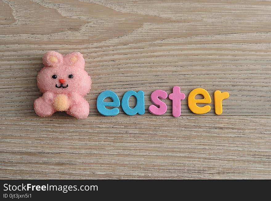 A pink bunny shape marshmallow with the word easter isolated on a wooden background