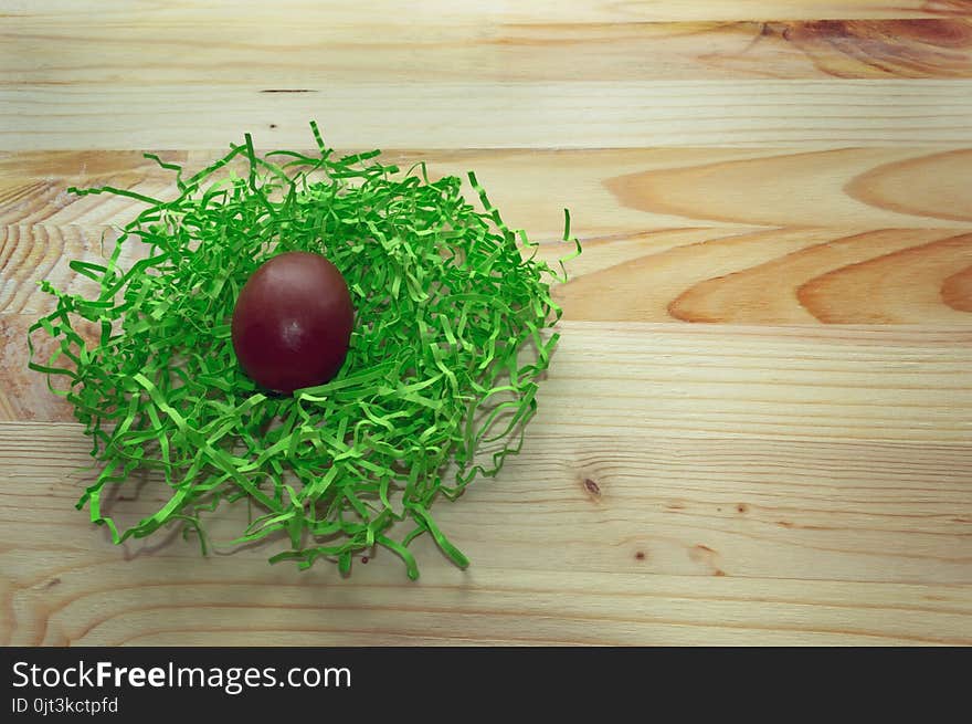 Chocolate egg in green nest on wooden background