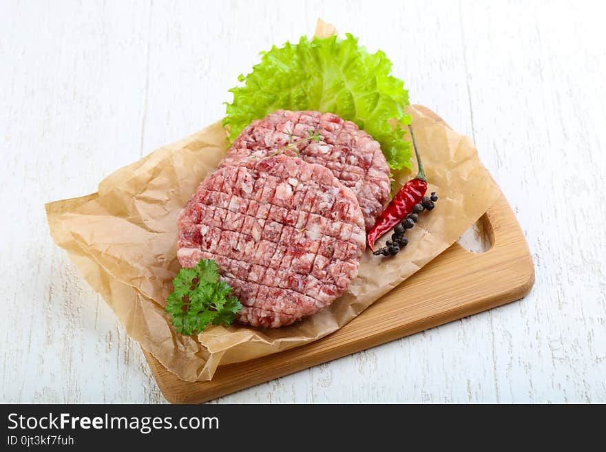 Raw burger cutlet with salad leaves and parsley
