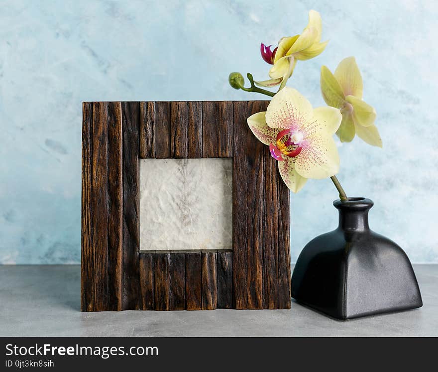 Wooden photoframe mockup with yellow orchid against light blue wall. Interior design concept. Text space