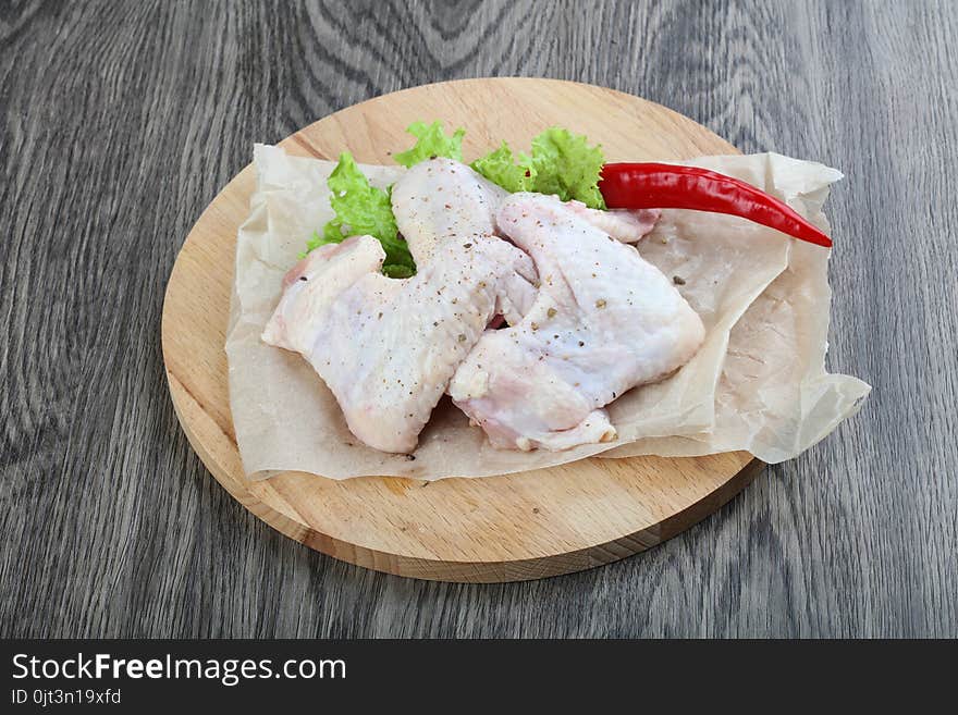 Raw chicken wings with salad leaves on wood background