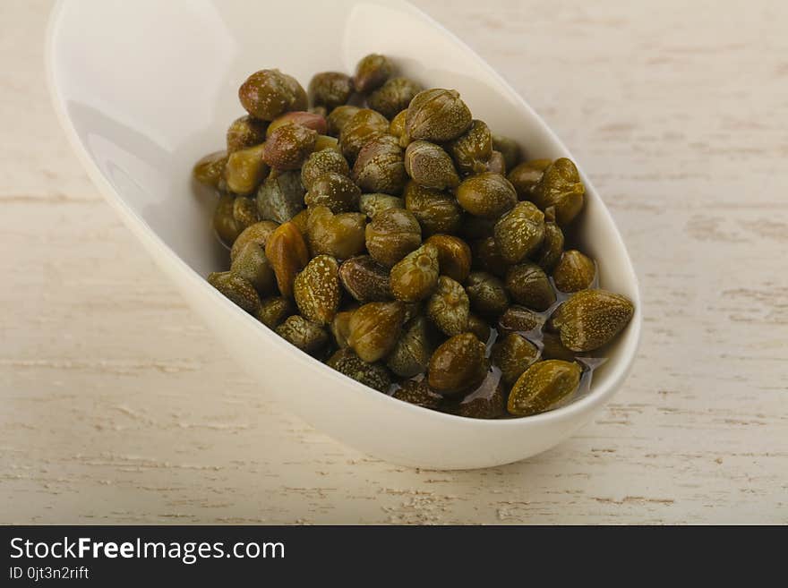 Marinated capers in the bowl over wood background. Marinated capers in the bowl over wood background