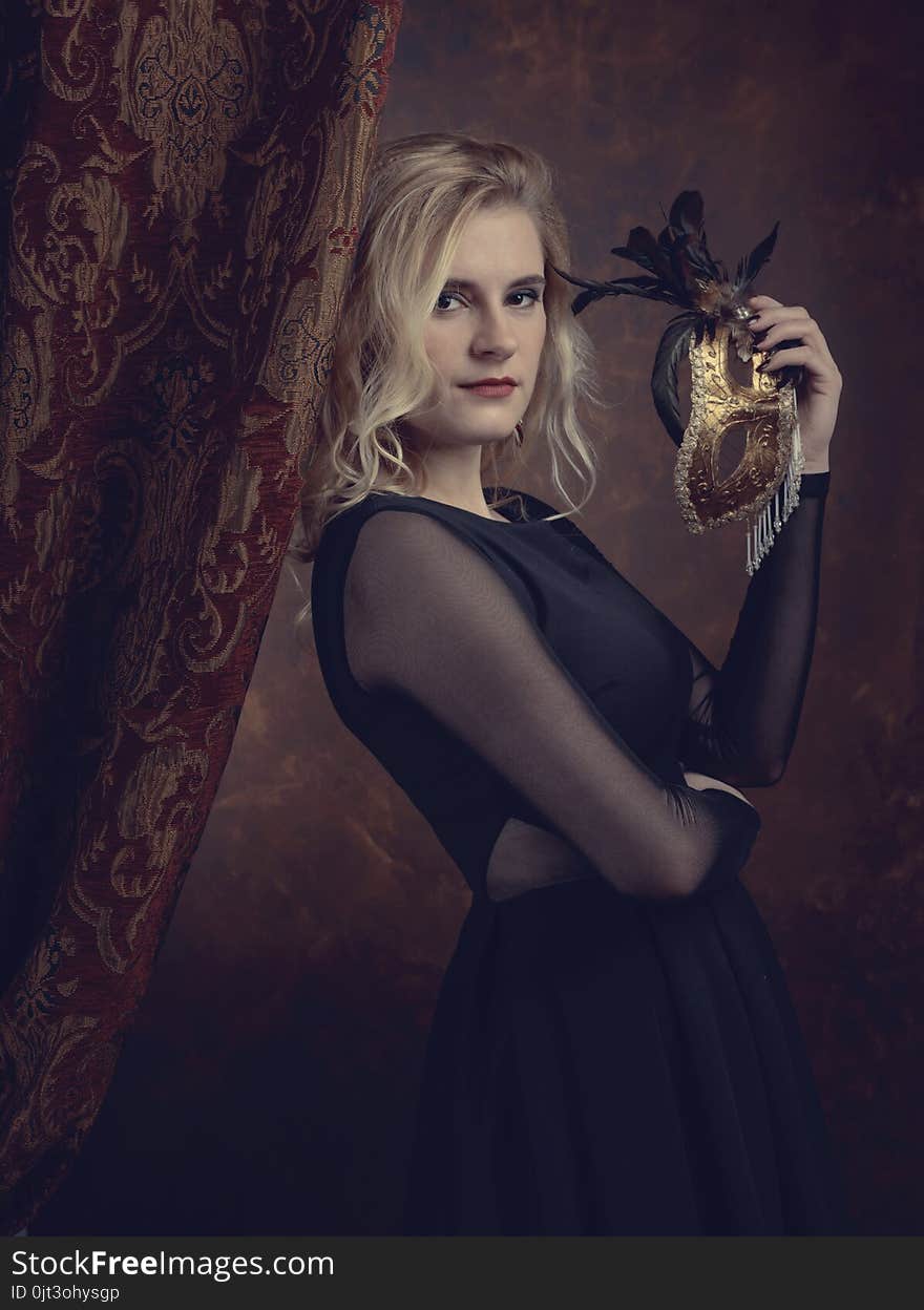 Portrait of beautiful young woman with carnival mask. Gorgeous hair and natural makeup. Fashion beauty photo. Natural blonde in black dress. Portrait of beautiful young woman with carnival mask. Gorgeous hair and natural makeup. Fashion beauty photo. Natural blonde in black dress.