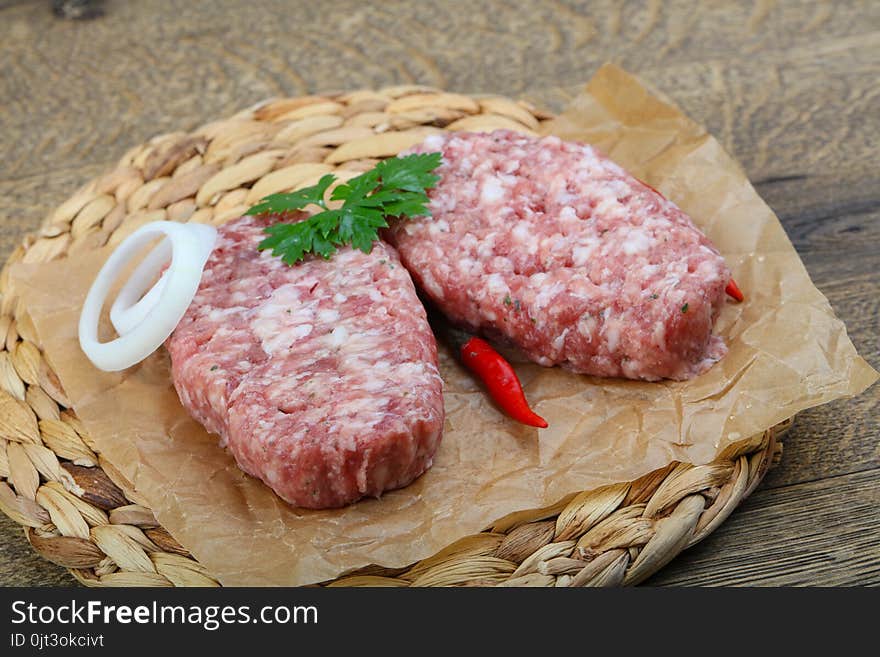 Raw burget cutlet with onion and parsley on wood background