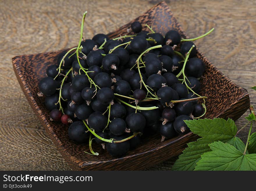 Black currants heap with leaves on wood background