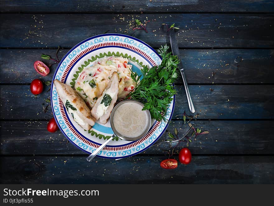 Chicken breast stuffed with spinach and cheese. On a beautiful plate with mashed potatoes and greens. On a colored wooden background with cutlery. Top view.