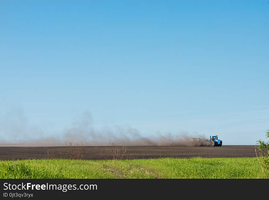 Blue tractor plowing field at sunny day