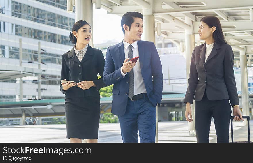 Team of business people smart men and women walk in rush hour at outdoor pedestrian walk way and talk together with tablet smart phone device and luggage with the city space building. Team of business people smart men and women walk in rush hour at outdoor pedestrian walk way and talk together with tablet smart phone device and luggage with the city space building