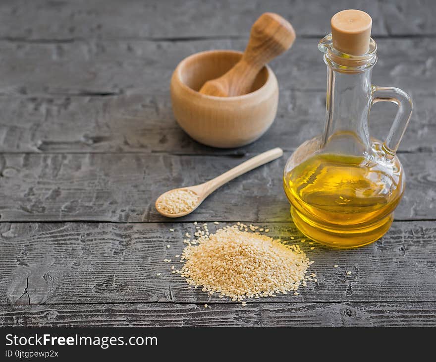 Sesame seeds, oil bottle and mortar with pestle on dark wooden table. Natural vegetarian food.