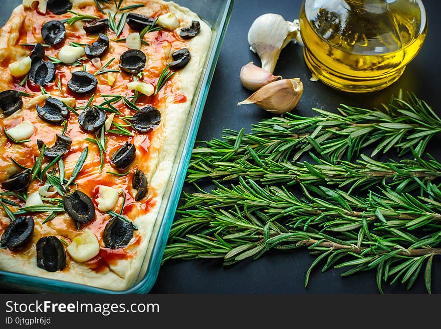 Dough for home made italian focaccia with rosemary and olives, ready for baking, on dark background. Dough for home made italian focaccia with rosemary and olives, ready for baking, on dark background