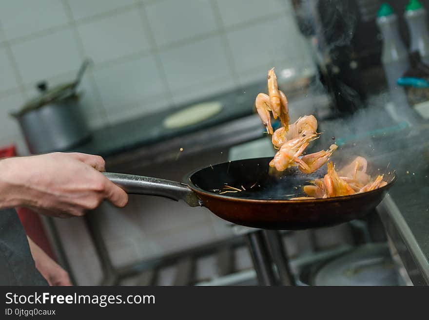 Chef At Work. Hand Holds A Hot Pan With Fried Shrimp. Process Of Preparation Of Shrimps.