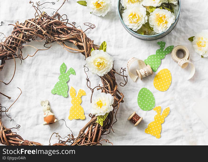 Homemade Easter wreath of vines with flowers, paper rabbits, ribbons on a white background, top view. Easter craft decorations home. Concept of creativity