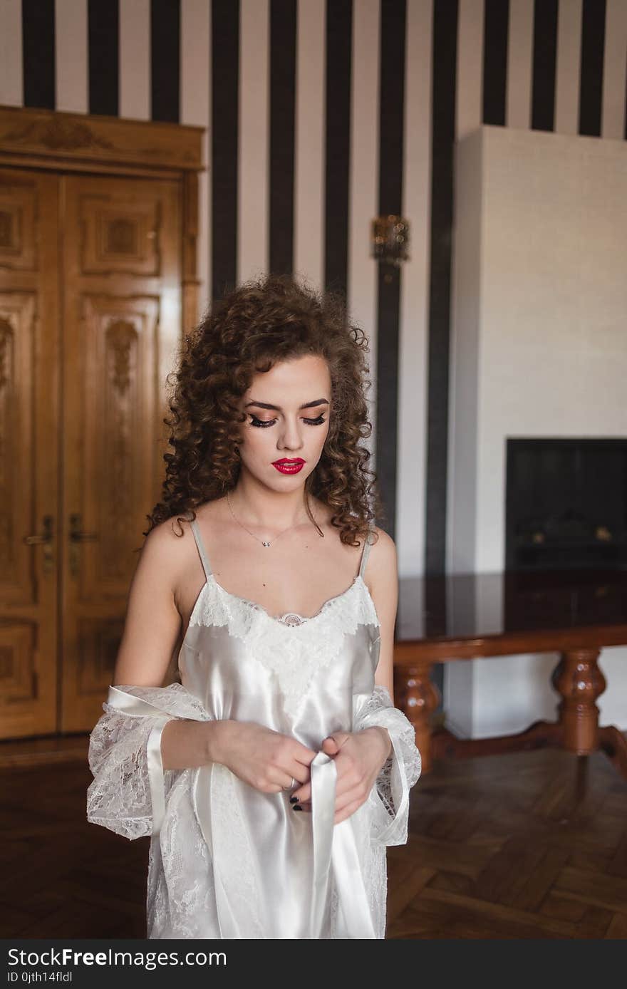 Beautiful pensive curly young woman in white bathrobe sitting and relaxing at home