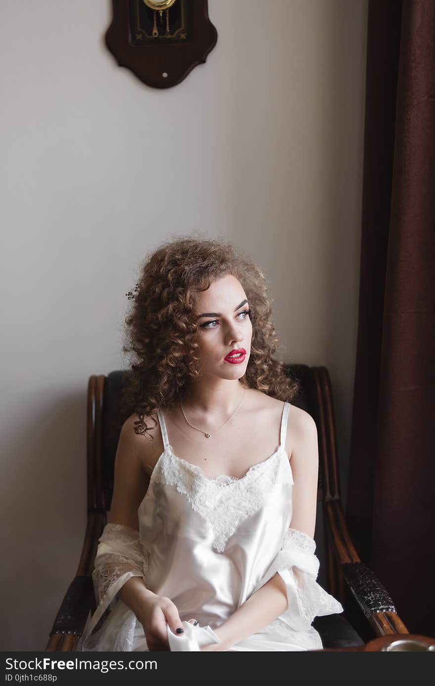 The curly-haired girl sits on an armchair at it the class figure and she is dressed in a dressing-gown