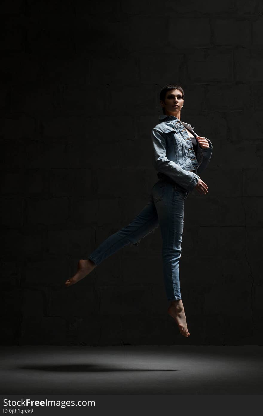 Ballet dancer with shot haircut in jeanswear jumping gracefully in dark room. Ballet dancer with shot haircut in jeanswear jumping gracefully in dark room