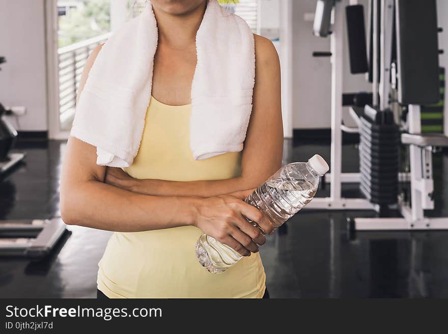 Fitness woman with white towel holding a bottle of water at gym