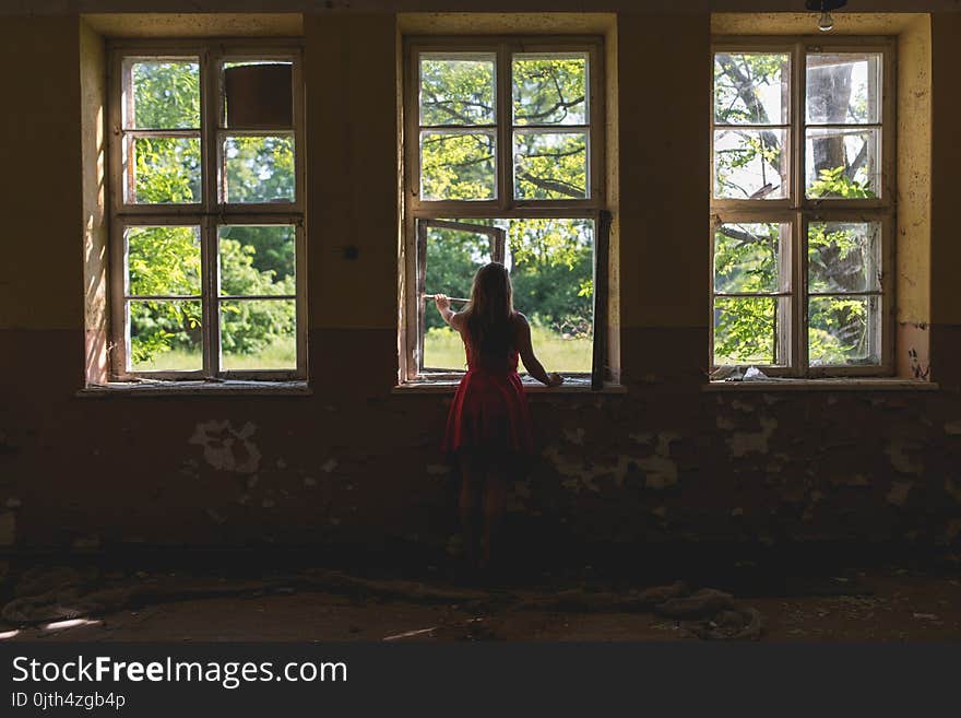 Woman in red dress looking through the window in the old building at summer sunny day