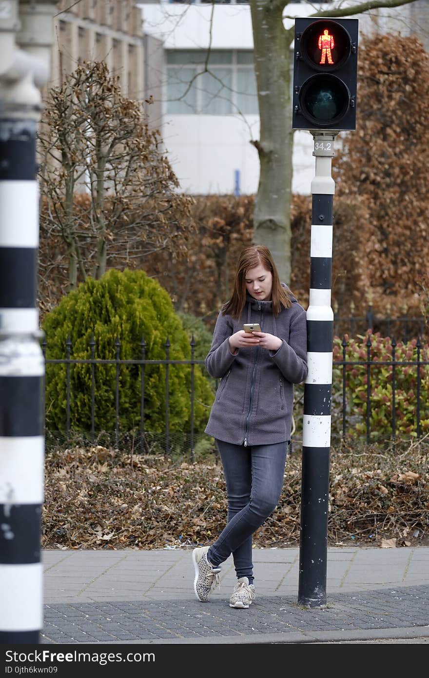 Young woman waits at a traffic light that is on red but does not pay attention to the traffic because she looks at her mobile phone. Young woman waits at a traffic light that is on red but does not pay attention to the traffic because she looks at her mobile phone.