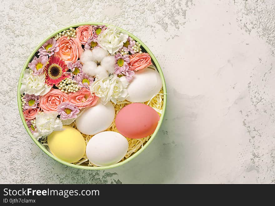 Painted and white easter eggs with flowers in a circle plate on a textured cement background, top view with copy space