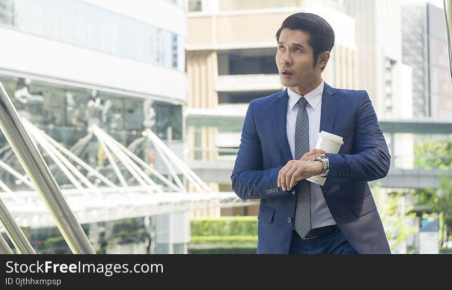 Business asia man stand with paper cup of drink at outdoor pedestrian stair walkway