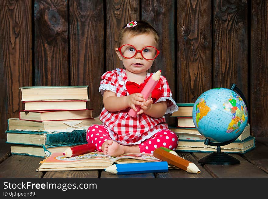 Happy a nice little girl with glasses and pencils against the background of books and a globe.