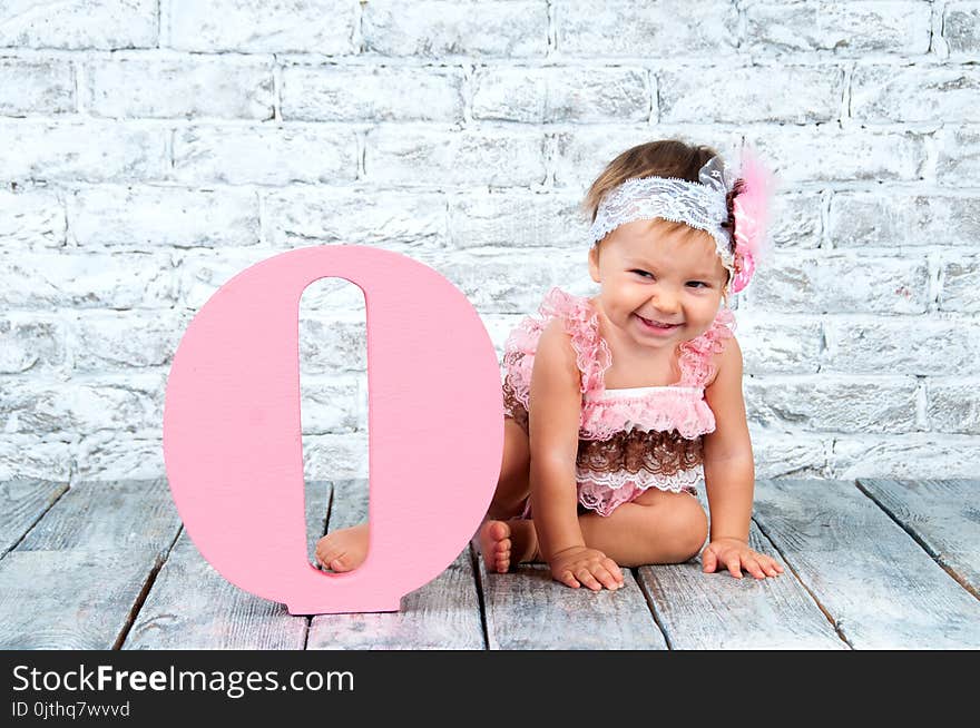 Beautiful and cute girl in a pink dress with the letter O. Emotional girl.