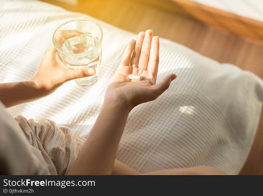 Woman with pills or capsules on hand and a glass of water