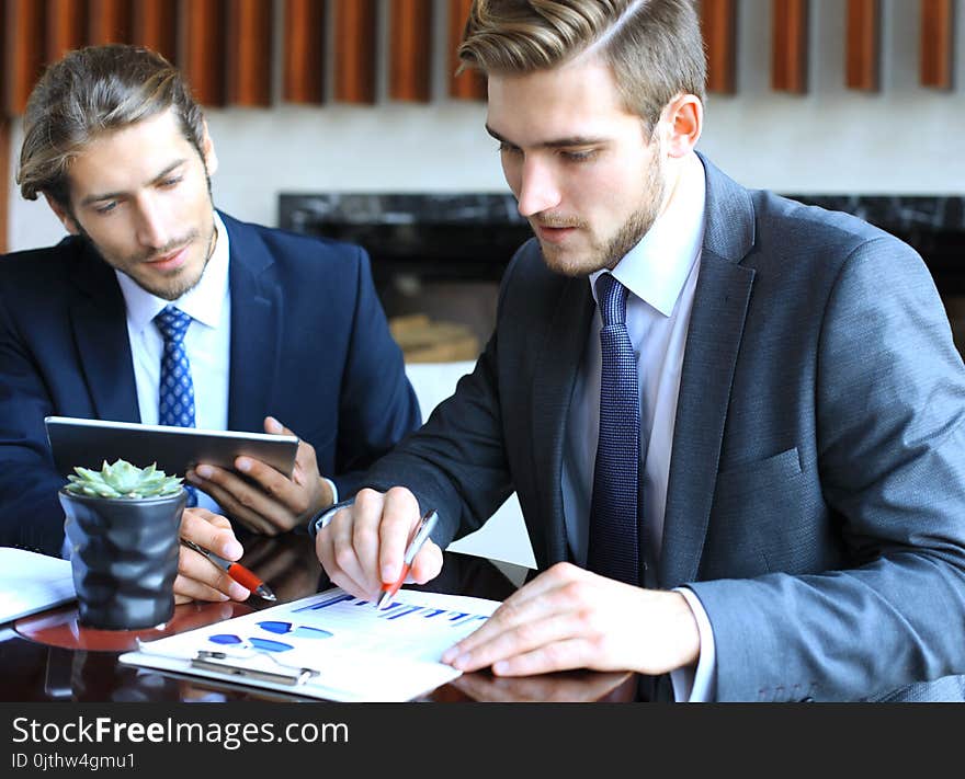 Two Young Businessmen Analyzing Financial Document At Meeting.