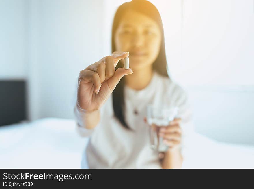 Woman With Pills Or Capsules On Hand And A Glass Of Water