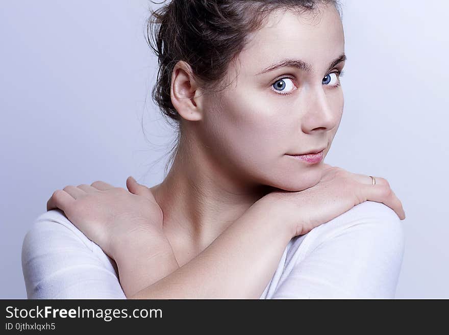 Portrait of young attractive caucasian girl on gray background. Gentle look of beautiful woman. The woman is looking at the frame, her head and arms are on her shoulders