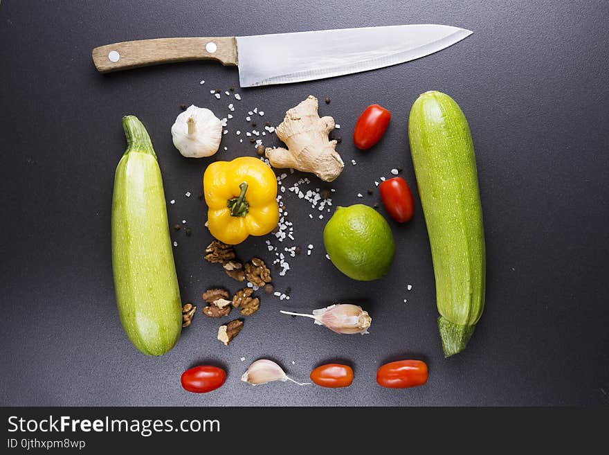 Vegetables and knife on black ceramic table. Ingredients for cooking. Zucchini, peppers, tomatoes, garlic, lime, nuts and sea salt. Healthy eating.