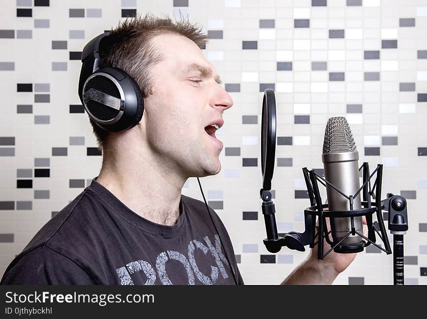 A young guy singer and rock musician sings in a studio condenser microphone in headphones in a recording studio. Record voice to microphone. Vocal is a rock musician.