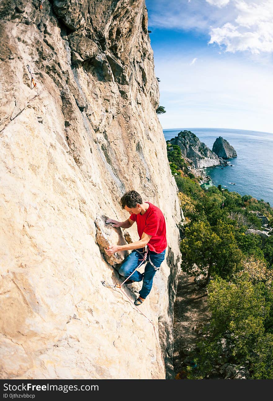 A rock climber on a rock. A man climbs the rock against the background of the sea coast. Active lifestyle. Sports in nature. Overcoming a difficult climbing route.