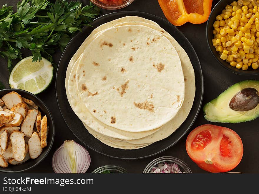 Tacos ingredients background with flatbread, fresh vegetables and roasted chicken meat on the table. Mexican fast food top view with copy space.