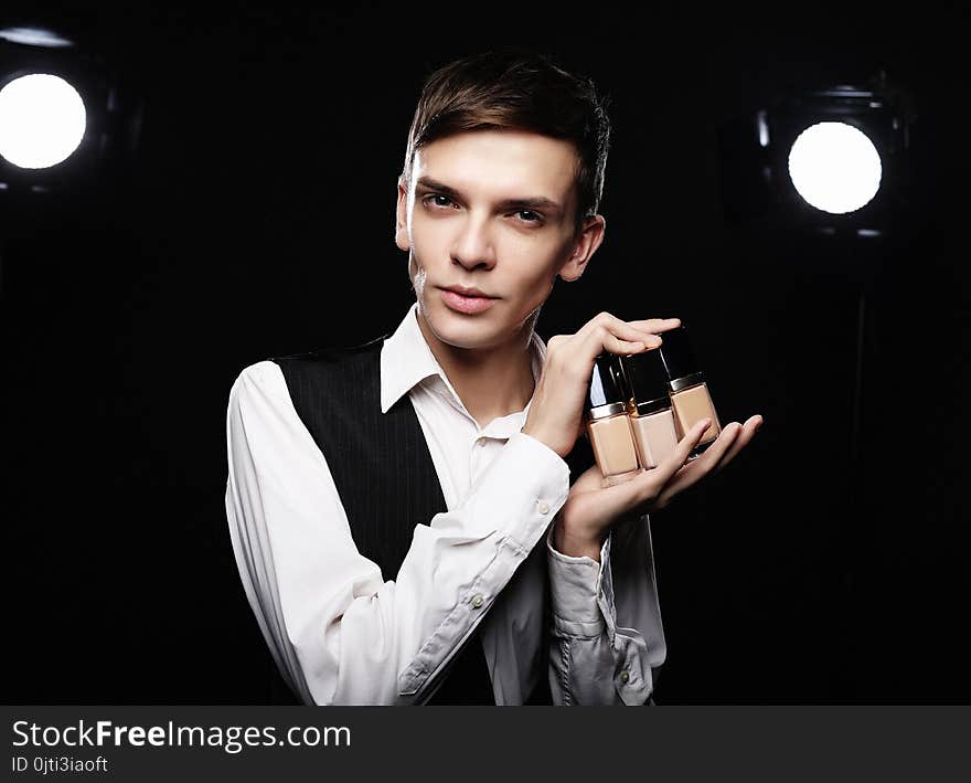 Beauty concept. Young male make up artist posing with foundation for make-up on a dark background.