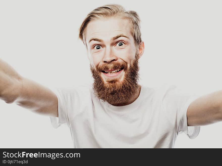 Close up portrait of a cheerful bearded man taking selfie over white background. Studio shoot.