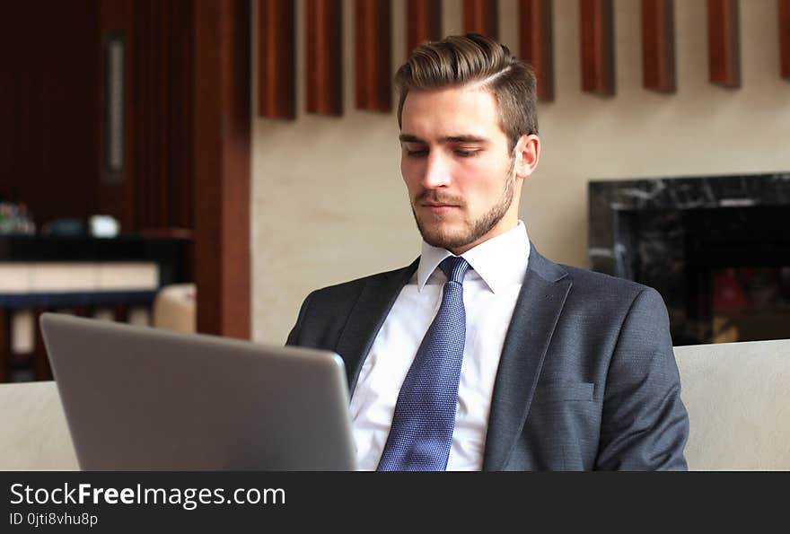 Young businessman working on laptop, sitting in hotel lobby waiting for someone.