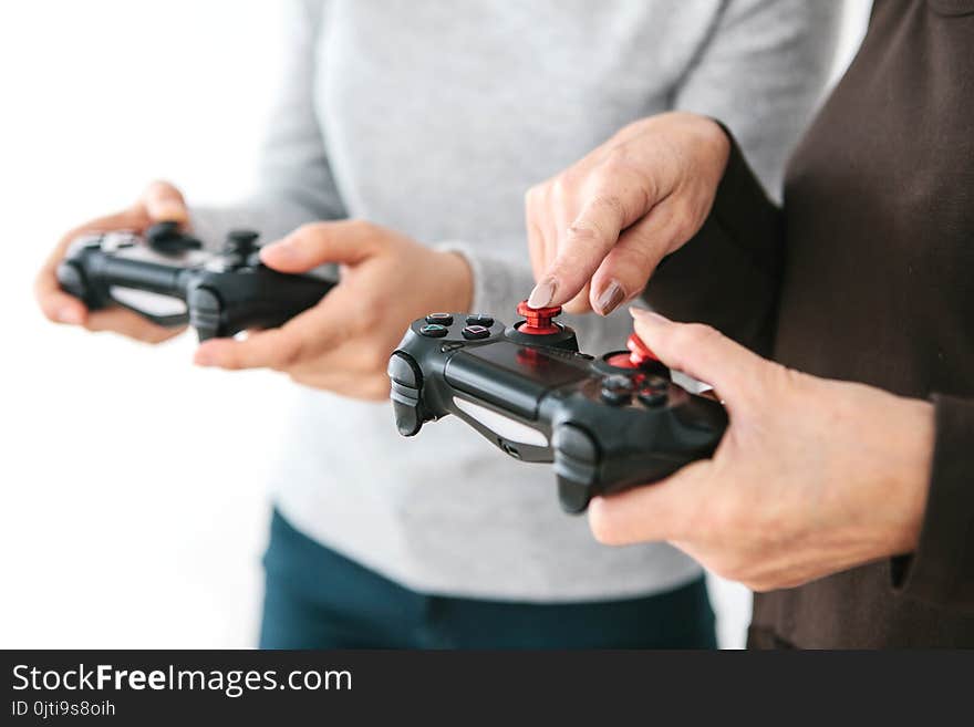 The elderly woman asks the young girl how to use the joystick for video games and shows her finger on the buttons. Modern technologies and people. Teaching older generation the use of technology