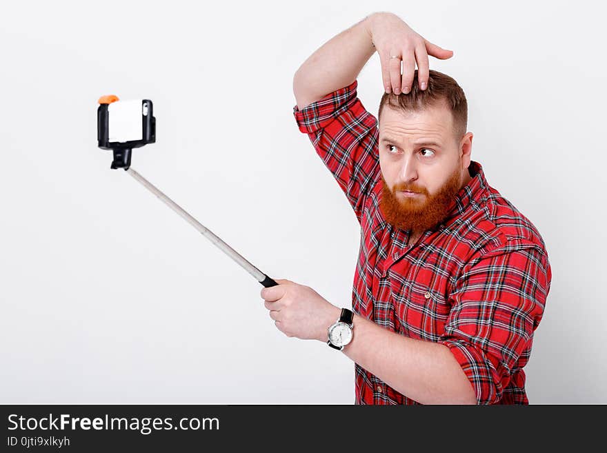 Man with red beard in plaid shirt makes selfie on phone. Man with red beard in plaid shirt makes selfie on phone