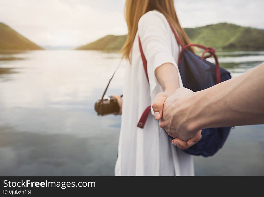 Young woman with camera holding man`s hand and leading him on nature outdoor, Couple vacation travel