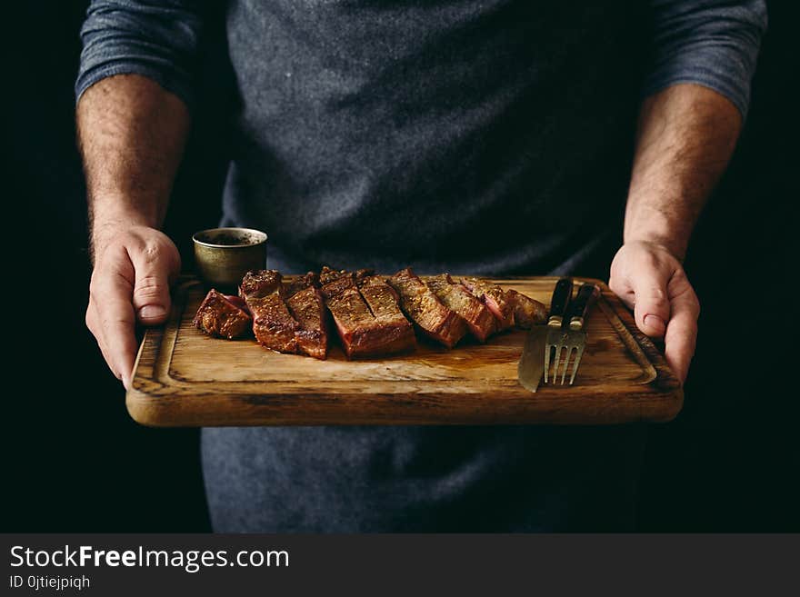 Man holding juicy grilled beef steak with spices on cutting board