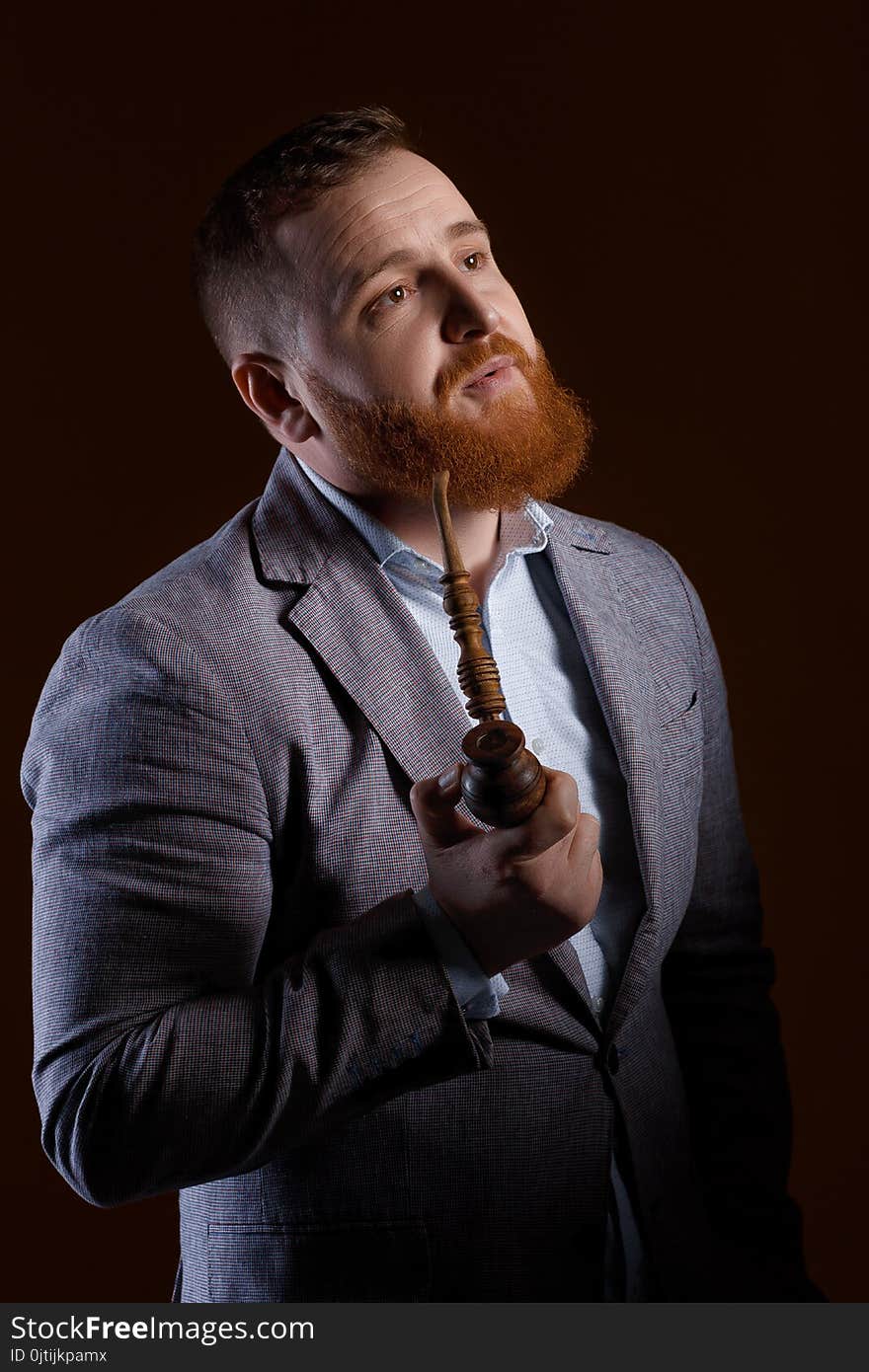 Portrait of a red bearded man smoking a pipe on a brown background